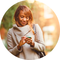 A woman stands outside and looks at her cellphone. 